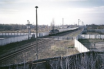 Ein Transitzug aus Hamburg durchfährt die Grenzanlagen am Bahnhof Berlin-Staaken, vor dem Zug der Bahnübergang für die DDR-Grenztruppen, 1986