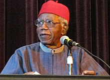 Achebe in red cap at lectern