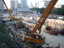 View of the construction site with construction machinery and vehicles, with a fence separating from the main road.