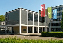 Haupteingang der Hochschule Hannover, Gebäude mit Logo der Hochschule und Fakultätsfahnen