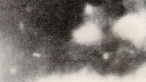 An enlargement of the Moorman photograph: the figure of a man can be hazily seen. He appears to be firing a gun, with bright muzzle flare obscuring his right side. He may be wearing a dark uniform, with a white object on his left chest.