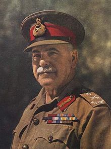 Head and shoulders colourised photograph of General Sir Thomas Blamey, GBE, KCB, CMG, DSO taken circa 1942. Blamey has a grey moustache and is wearing a peaked cap with scarlet cap band and general's bullion cap badge and an Australian Army khaki shirt to which are attached Australian general's embroidered rank slides, general's gorget patches in scarlet with gold bullion oakleaves and three ribbon bar rows for his various orders, decorations and medals.