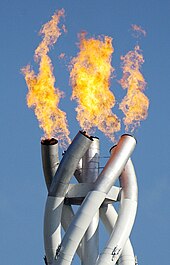 Photographie d'une torche en flamme, à trois bras entrelacés.