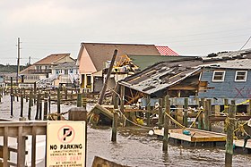 An image of multiple damaged buildings along a dock; one has collapsed on itself.