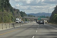A freeway with four lanes divided by a concrete barrier, looking towards a bridge in the distance.