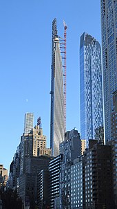 111 West 57th Street as seen in December 2019 from Columbus Circle. There is a construction crane on one side of the building. From left to right, 432 Park Avenue, the sign above the Essex House, One57, and 220 Central Park South can be seen in the background.