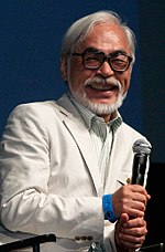 Hayao Miyazaki holding a microphone and laughing