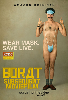 Baron Cohen as Borat in a slingshot swimsuit in the style of a surgical mask, smiling and giving thumbs up. Text surrounding him says "WEAR MASK. / SAVE LIVE.".
