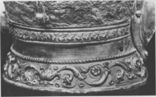 Black and white photograph of the neck guard of the Emesa helmet, showing the three layers of decoration: a torus of ivy leaves bordered by cords at the top, a smooth silver section in the middle, and an acanthus scroll decoration at the bottom.