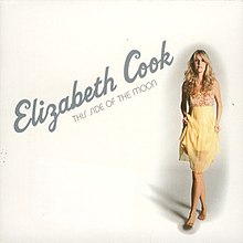 An image of a blonde woman standing in front of a white background. She is wearing a yellow dress, and the words "Elizabeth Cook" and "This Side of the Moon" are included in different colored fonts.