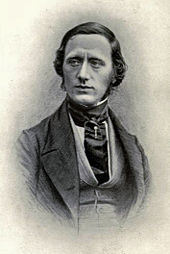 photograph of a manm, facing spectator but looking down, dressed in mid-Victorian style with broad silk tie and tie-pin