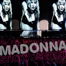 The upper part shows three similar image of a blond woman, wearing a black bra. Her right hand is held up. The lower part shows a crowd looking at her. On top of them, the words "MADONNA" and "STICKY & SWEET TOUR" is written.