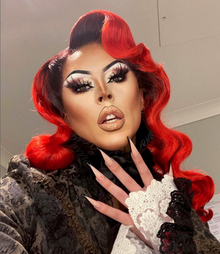 Photograph of a drag queen wearing a red wig and black outfit