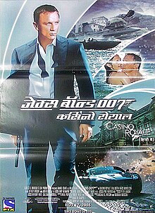 A man in a business suit with a loose tie holding a gun. Behind him is a building with a sign reading "Casino Royale", and a woman in a black dress who stands on the entrance staircase. At the bottom of the image is the title "Casino Royale" – both "O"s stand above each other, and below them is a 7 with a trigger and gun barrel – and the credits.