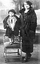 Un bambino in piedi su di una sedia accanto alla madre.